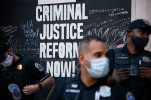 Police officers stand in front of sign that reads "Criminal Justice Reform Now!"