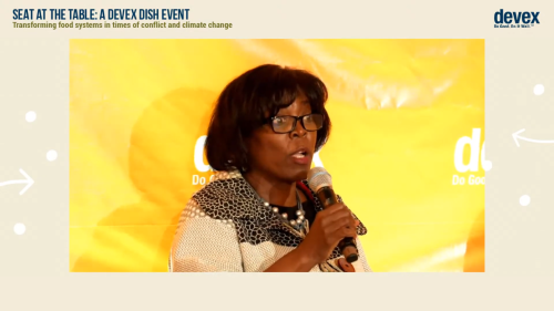 Screenshot of Ertharin Cousin speaking in front of a yellow background into a microphone 