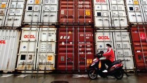 A woman rides her motorcycle past containers at the Port of Shanghai.