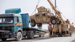 US military vehicles being loaded onto a flatbed pickup truck by a crane
