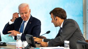 President Biden and French President Emmanuel Macron exchange words at a table with microphones.