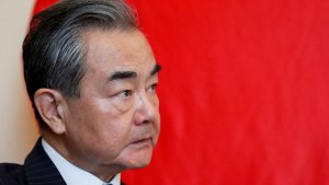 Profile head shot of Wang Yi looking to his left in front of a red Chinese flag.