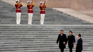 Xi and Macron walk next to steps with trumpeting guards in red. 