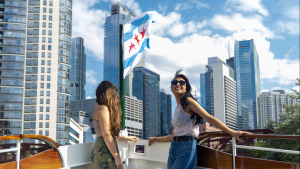 Two people at the front of a boat with the Chicago skyline behind them.