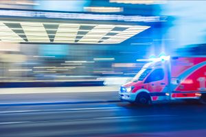 An ambulance drives past a hospital; background is blurred
