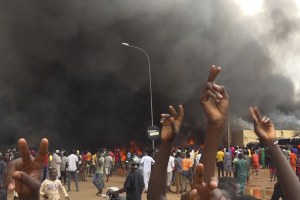 With the headquarters of the ruling party burning in the back, supporters of mutinous soldiers demonstrate in Niamey, Niger, Thursday, July 27 2023.