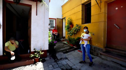 A woman in a mask holds a baby in front of her house in Chile.