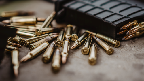 Gold bullets in a pile on grey surface next to black magazine.