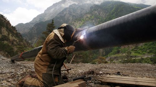 A welder works on a pipe with mountains in the background