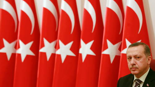 Turkish President Recep Tayyip Erdogan sits in front of a row of Turkish flags.
