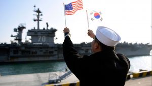 A ROK sailor waves flags in front of an aircraft carrier