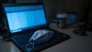 A laptop computer with a medical mask sitting on it.