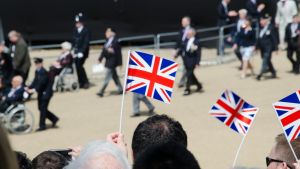 People wave small British flags while a crowd of people walks by in the background