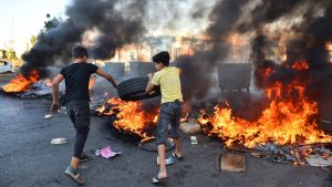 Protestors in Lebanon run through a street with fire in the background