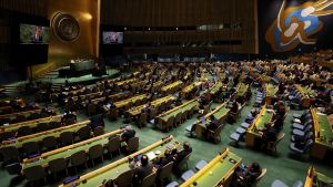 The UN Security Council assembles in rows of chairs in a dark room with green floors.