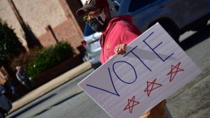 A person wearing a surgical face mask holds a sign saying "VOTE"