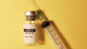 A shot and a bottle saying "VACCINE COVID-19" with a yellow background