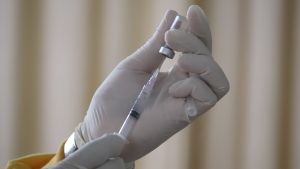 A person wearing surgical gloves prepares a vaccine shot