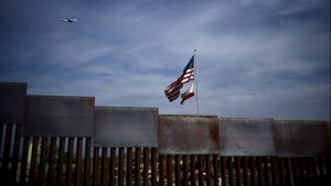 American and California state flags fly behind the US-Mexico border wall